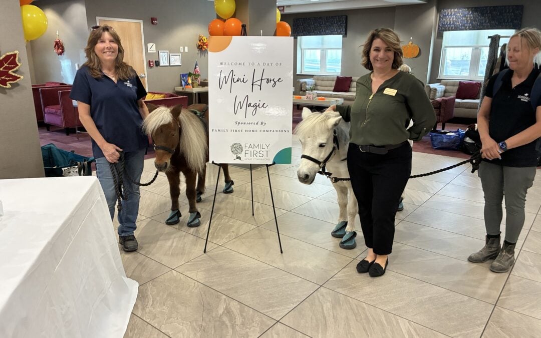Family First Home Companions team with two miniature horses beside the Mini Horse Magic welcome sign at The Five Towns Premier